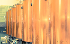 Image is a close up shot of seven brass kettles in a row