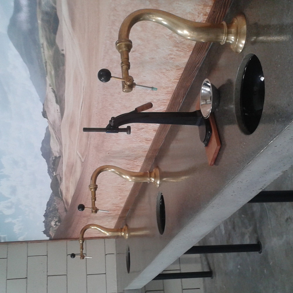 Image is of three brass taps with a black bottle capper and a picture of a wheat field